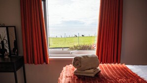 A room with a bed, a window with curtains, and a view of a green field and fence. - North Coast Cottage - Coastal Highland Retreat with Sea Views (Portgower)