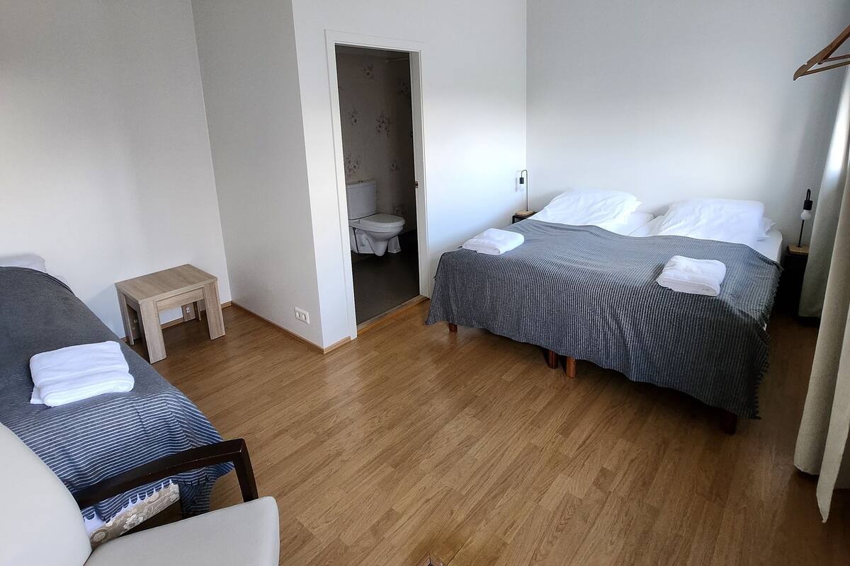 Ein Hotelzimmer mit zwei Betten, einem kleinen Tisch, einem Stuhl und einem durch eine offene Tür einsehbaren Badezimmer.