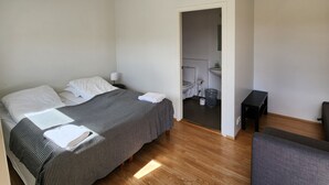 Una habitación de hotel moderna con una cama grande, un pequeño sofá, piso de madera y un baño visible a través de una puerta abierta.