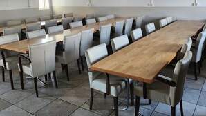 Un salón de conferencias con una larga mesa de madera y sillas blancas, suelo de baldosas y paredes blancas.