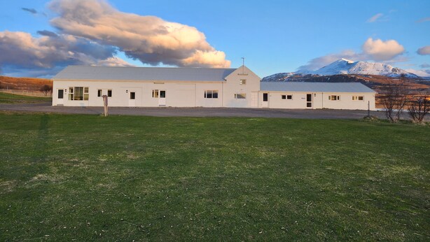 Un edificio blanco con varias ventanas y techo plano, con cielo despejado y una montaña nevada a lo lejos.