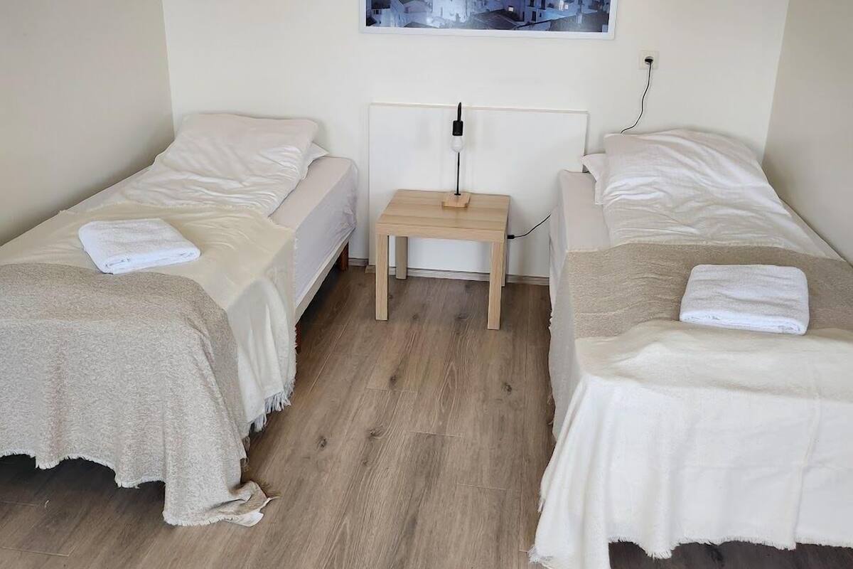 Ein kleiner, sauberer Raum mit zwei Einzelbetten, einem Nachttisch, einer Lampe und einem Bild an der Wand.