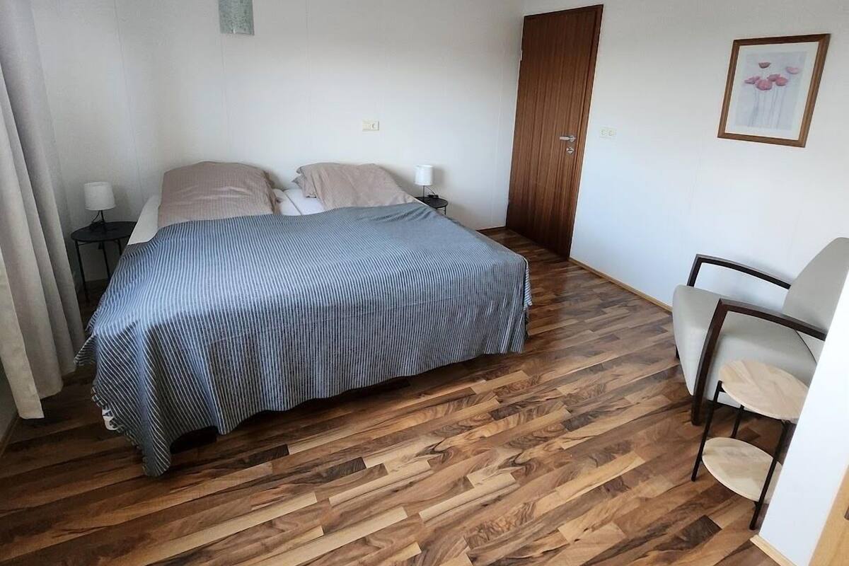 Ein Schlafzimmer mit einem Bett, Holzboden, einem Sessel und einer Tür.