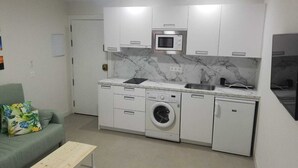 Een kleine keuken met een magnetron, gootsteen, wasmachine en een compacte koelkast.