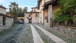 A narrow cobblestone street flanked by stone buildings with balconies, a parked car, and lush greenery. - 1 bedroom gorgeous home in Baveno (Baveno)