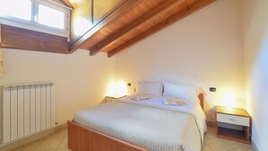 Ein Schlafzimmer mit Holzboden, einem Bett mit weißer Matratze und Kissen, einem Nachttisch mit Lampe und einem Heizkörper.