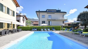 Ein Schwimmbecken mit Liegestühlen, ein Gebäude mit Balkon und eine Bergkulisse.