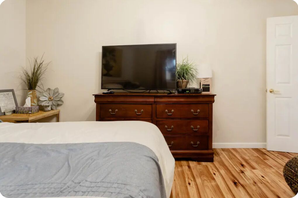 A bedroom with a bed, a wooden dresser, a television, and a door.