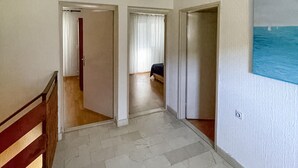 Käytävä, jossa on puinen kaide, laatoitettu lattia ja seinällä meriaiheinen maalaus.