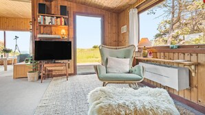A cozy cabin interior with a television, bookshelves, a comfortable chair, and a view of the outdoors. - Lovely home in Hundested with WiFi (Hundested)