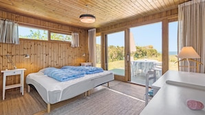 A wooden cabin bedroom with a bed, bedside tables, a desk, and a view of the outdoors. - Lovely home in Hundested with WiFi (Hundested)