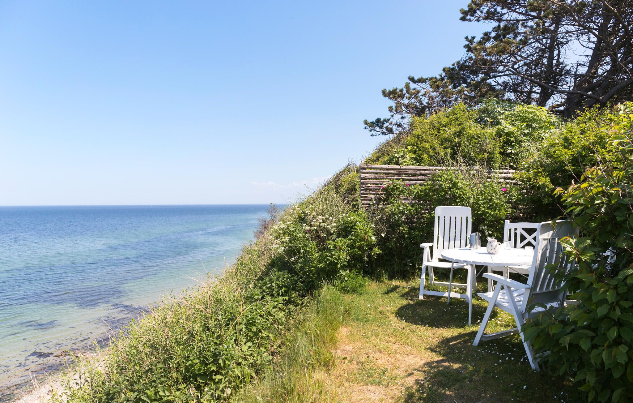 A coastal outdoor seating area with white chairs and a table, overlooking the sea.