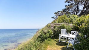 A coastal outdoor seating area with white chairs and a table, overlooking the sea. - Lovely home in Hundested with WiFi (Hundested)