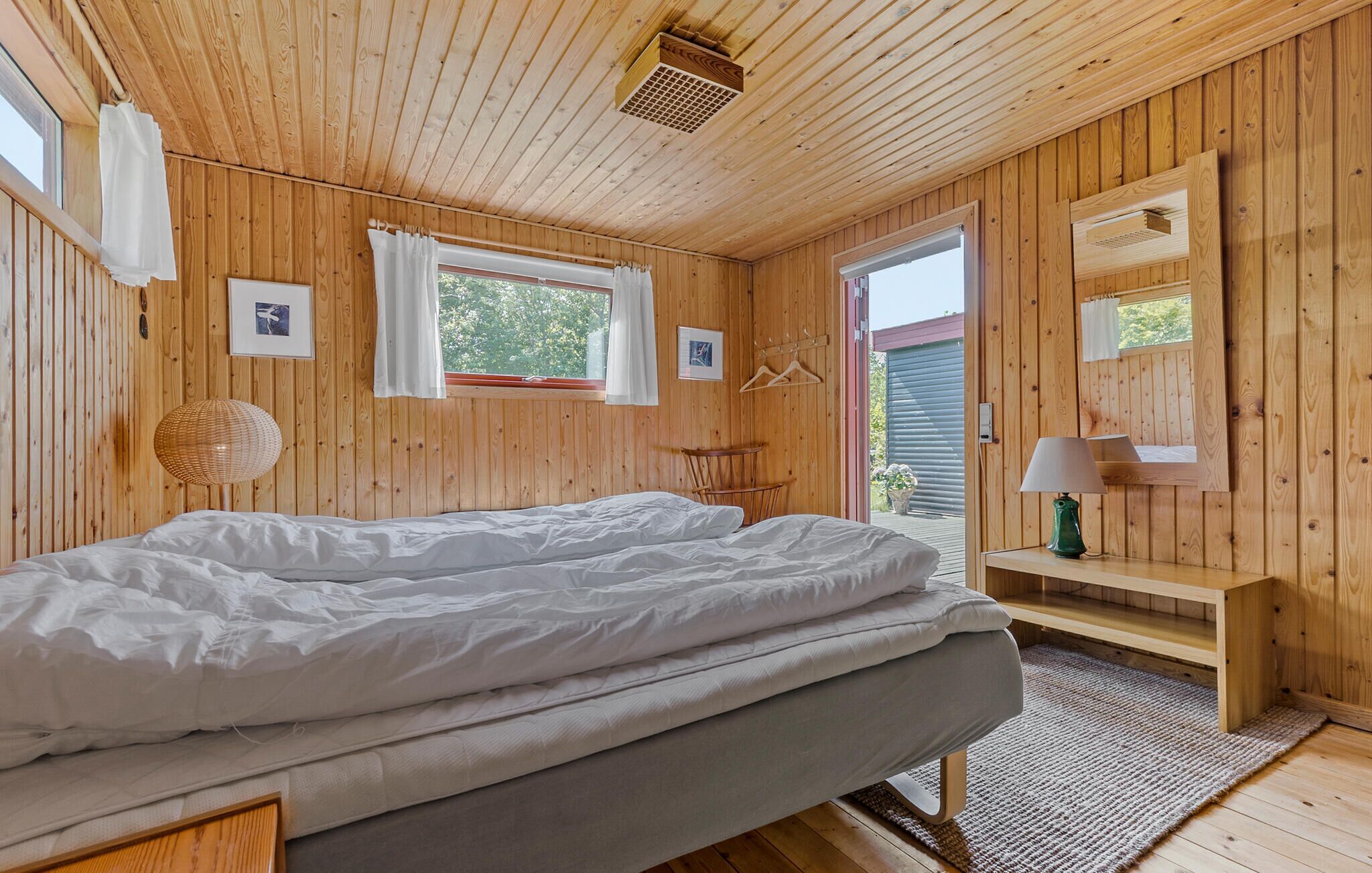 Ein Holzhütten-Zimmer mit einem Bett, einem kleinen Tisch, einer Hängelampe und einem Fenster.