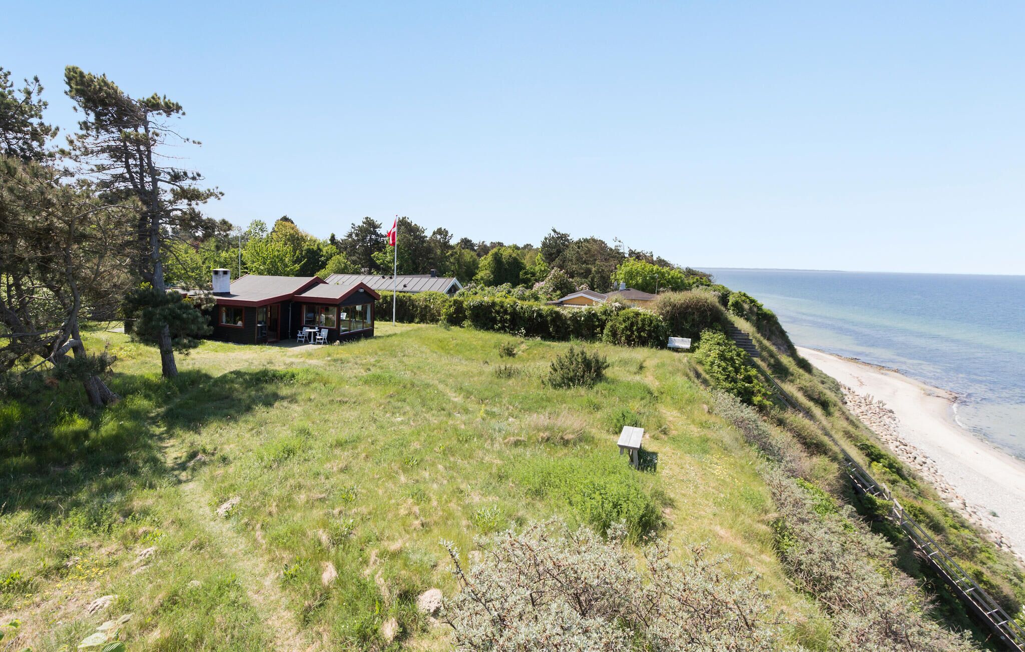Propiedad costera con un edificio principal y una estructura más pequeña, rodeada de exuberante vegetación y una playa.