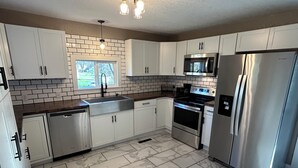 A modern kitchen with white cabinets, stainless steel appliances, a marble floor, and a window with a view of trees. - Beautiful Home in Gallatin (Gallatin)