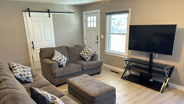 A living room with two grey sofas, a matching ottoman, a black TV stand, and a window with blinds. - Beautiful Home in Gallatin (Gallatin)