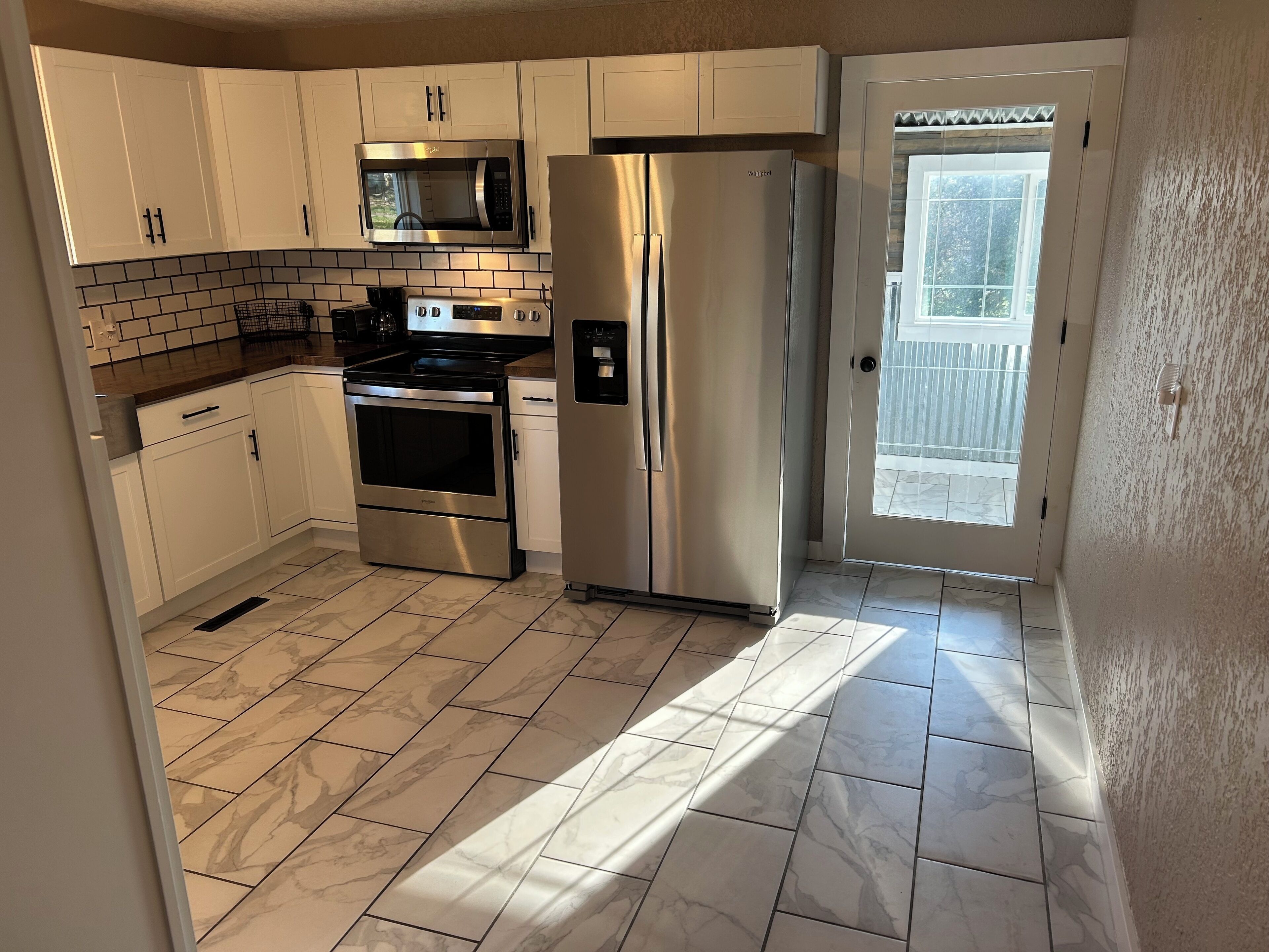 A kitchen with white cabinets, a stainless steel refrigerator, a microwave, and an oven.