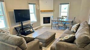 A living room with a flat-screen TV, a fireplace, a dining table with chairs, and two sofas with ottomans. - Beautiful Home in Gallatin (Gallatin)