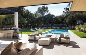 Un área junto a la piscina con sillones de descanso, un bar y un muro de piedra.