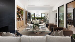 Un salon moderne avec une table basse en verre, des canapés blancs et un coin repas doté d’une table ronde.