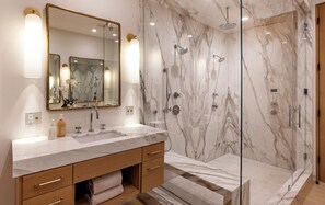 Un baño con ducha de mármol, un espejo grande y un tocador con lavabo y espacio de almacenamiento.