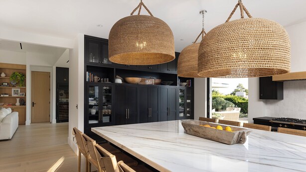 Une cuisine moderne avec des meubles de couleur sombre, un îlot en marbre et des suspensions lumineuses en fibres tressées.