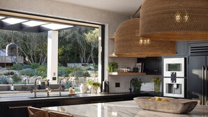 Une cuisine moderne dotée d’un grand îlot central, d’appareils électroménagers en acier inoxydable et offrant une vue sur un jardin aménagé.