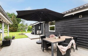 Eine Terrasse mit Tisch und Stühlen, einem Sonnenschirm und einem Haus im Hintergrund.