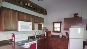 A kitchen with wooden cabinets, a white microwave, a stove, a sink, and a refrigerator.