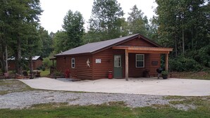 A wooden cabin with a porch, a sign reading "Little Mountain Cabins," and a small outdoor grill.
