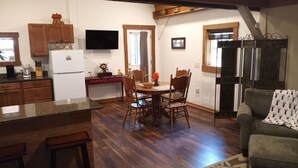A kitchen with wooden cabinets, a refrigerator, a dining table with chairs, and a television mounted on the wall.