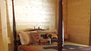 A wooden cabin bedroom with a four-poster bed, a ceiling fan, and a rustic decor.