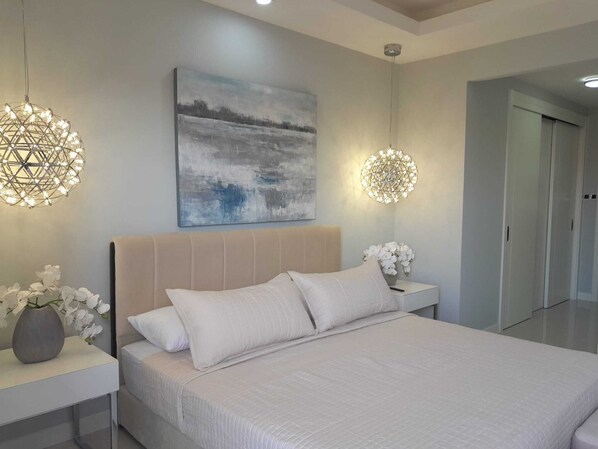 A modern bedroom with a large bed, two bedside tables, a wall-mounted abstract painting, and two unique spherical light fixtures.