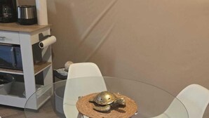 Una mesa de vidrio redonda con cuatro sillas blancas y un camino de mesa tejido.
