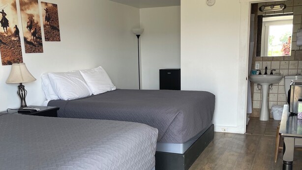 Habitación de hotel con dos camas, un escritorio, una lámpara, un altavoz negro pequeño y un baño visible a través de una puerta abierta.