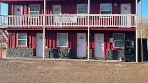 Un motel de dos pisos con fachada roja y detalles blancos. Cuenta con un letrero que indica un servicio de reservas de habitaciones de motel con un número de teléfono.