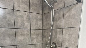 Zona de ducha con bañera blanca, paredes con azulejos grises y ducha.