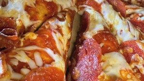 Primer plano de una pizza con pepperoni y queso derretido.