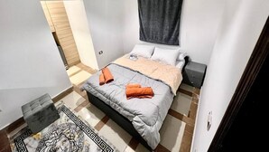 A bedroom with a bed, a nightstand, a lamp, a ceiling light, and a patterned rug. - NEAR THE PYRAMIDS INN 
5 minutes from the Great Pyramids of Giza & Sphinx!  (Giza)