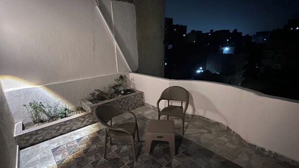 A balcony with two chairs and a small table, a planter with plants, and a view of the city at night. - NEAR THE PYRAMIDS INN 
5 minutes from the Great Pyramids of Giza & Sphinx!  (Giza)