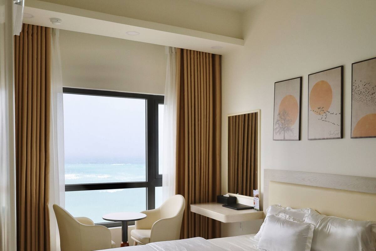 A hotel room with a large bed, a desk, a chair, and a view of the ocean.