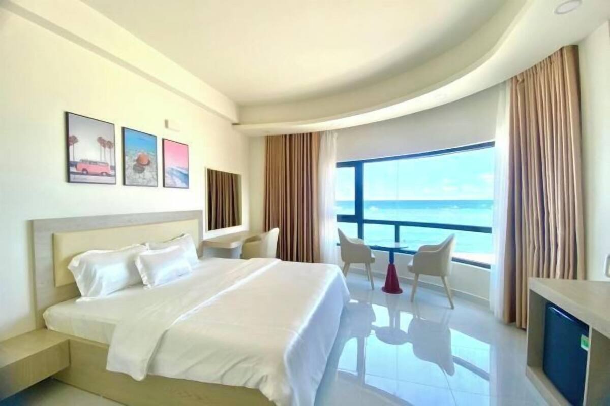 A hotel room with a bed, a desk, a chair, a TV, and a large window with a view.