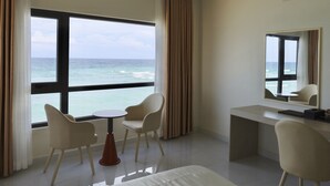 A hotel room with a large window offering a view of the ocean, a bed, a desk, and two chairs. - Island Sunset Hotel (Phu Quy)
