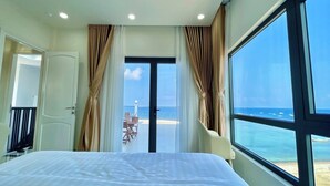 A bedroom with a large bed, a view of the beach, and a balcony with a table and chairs. - Island Sunset Hotel (Phu Quy)