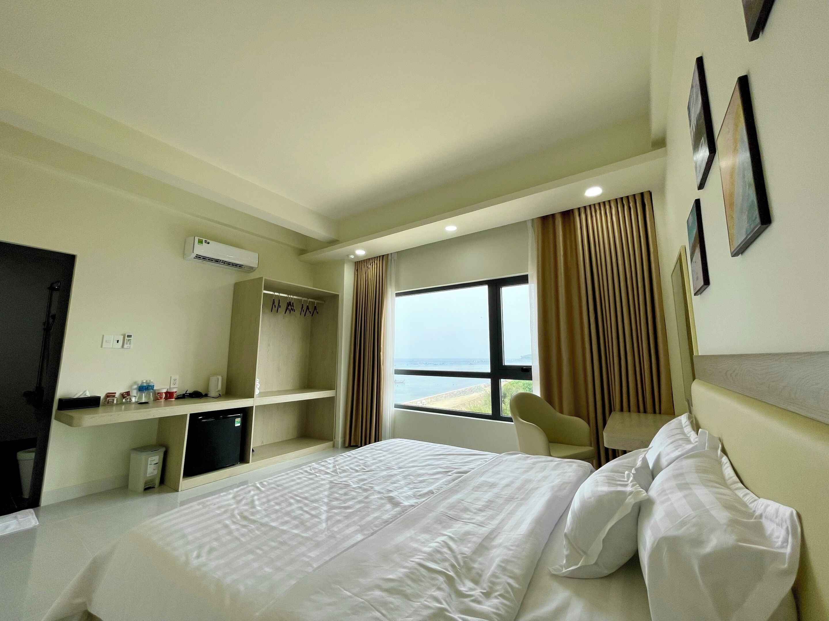 Habitación de hotel con cama, escritorio, silla, armario y un amplio ventanal con vistas al mar.