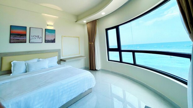A modern hotel room with a large bed, a view of the sea, and artwork on the wall. - Island Sunset Hotel (Phu Quy)