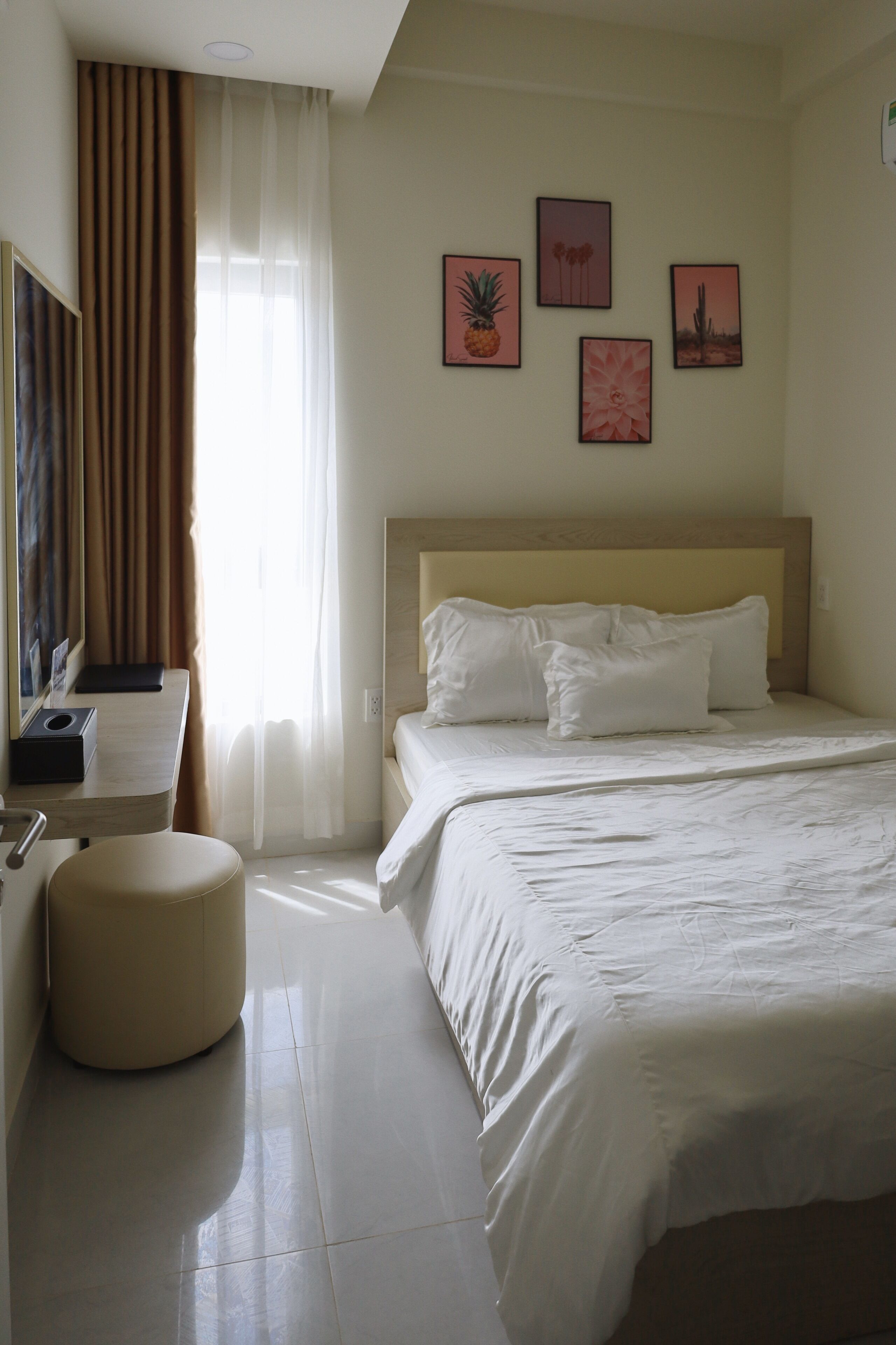 A hotel room with a bed, a desk, a chair, a round ottoman, and a large window with curtains.