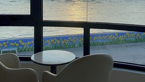 A room with a large window overlooking a sunset over the sea, a small round table, and two chairs. - Island Sunset Hotel (Phu Quy)