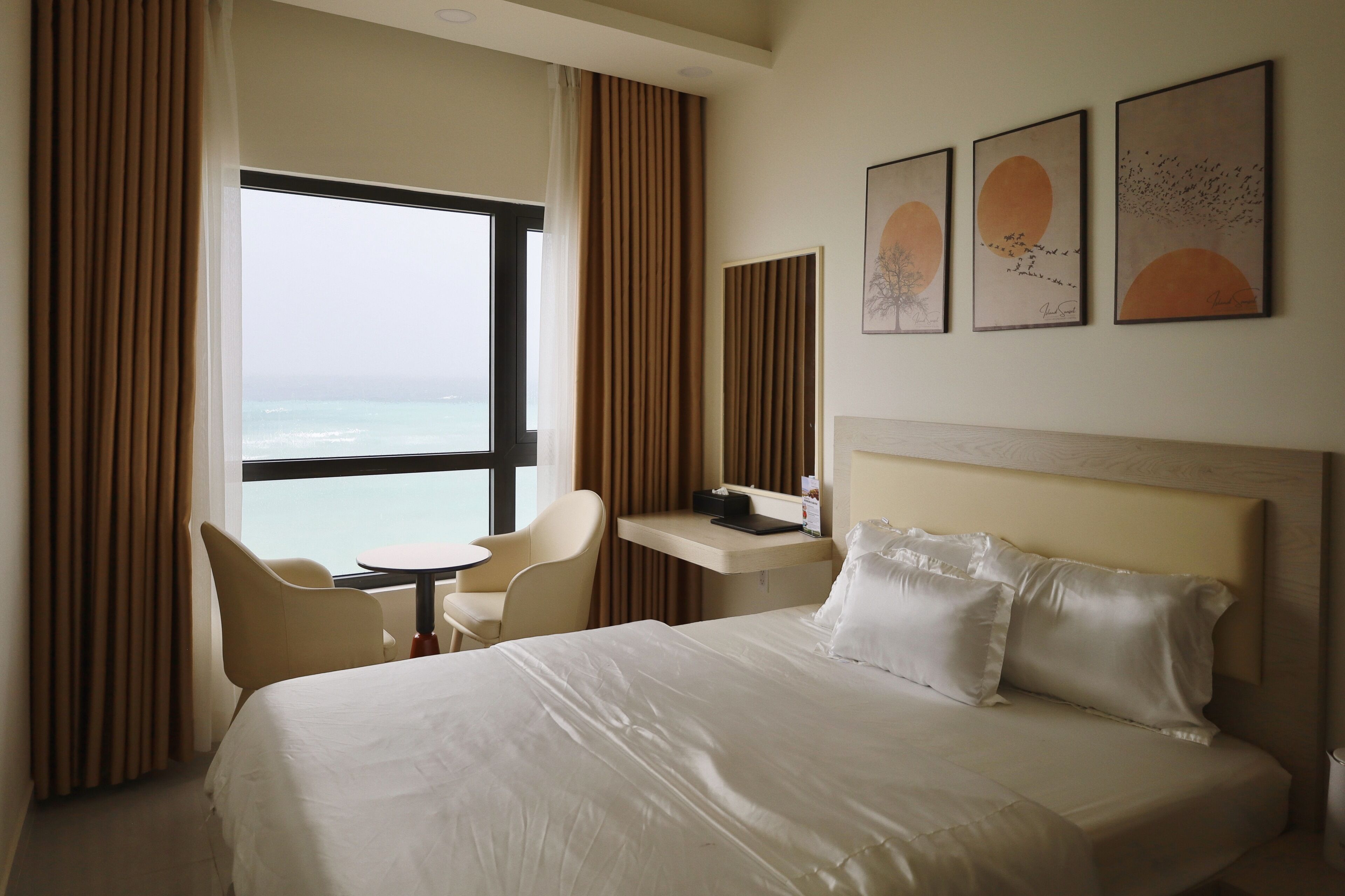 A hotel room with a large bed, a desk, a chair, and a view of the sea.